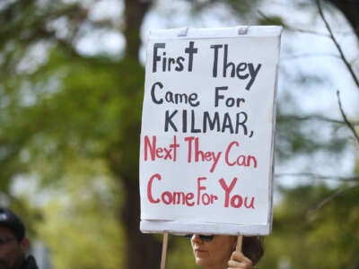 A protester holds a sign reading "FIRST THEY CAME FOR KILMAR, NEXT THEY CAN COME FOR YOU" during an outdoor protest